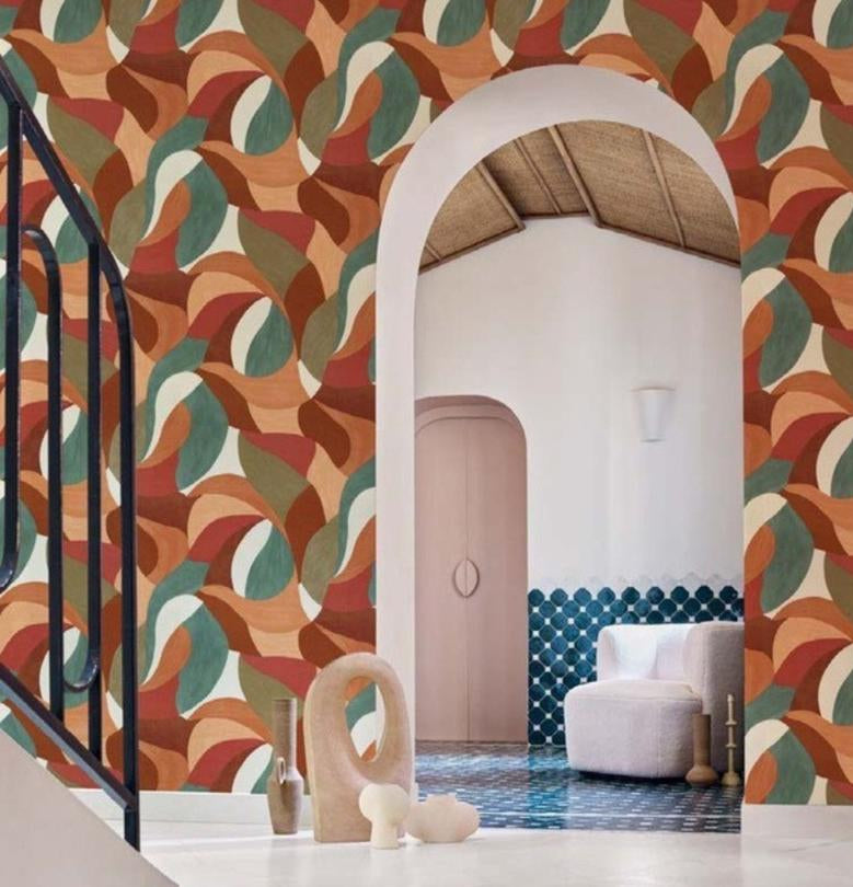 A wallpaper product presentation showing a patterned wall in a styled interior on the left and a dark product panel on the right labeled 'Mandela' with swatches and dimensions. The wallpaper pattern features overlapping abstract leaf-like shapes in rust, beige, teal, and brown tones.
