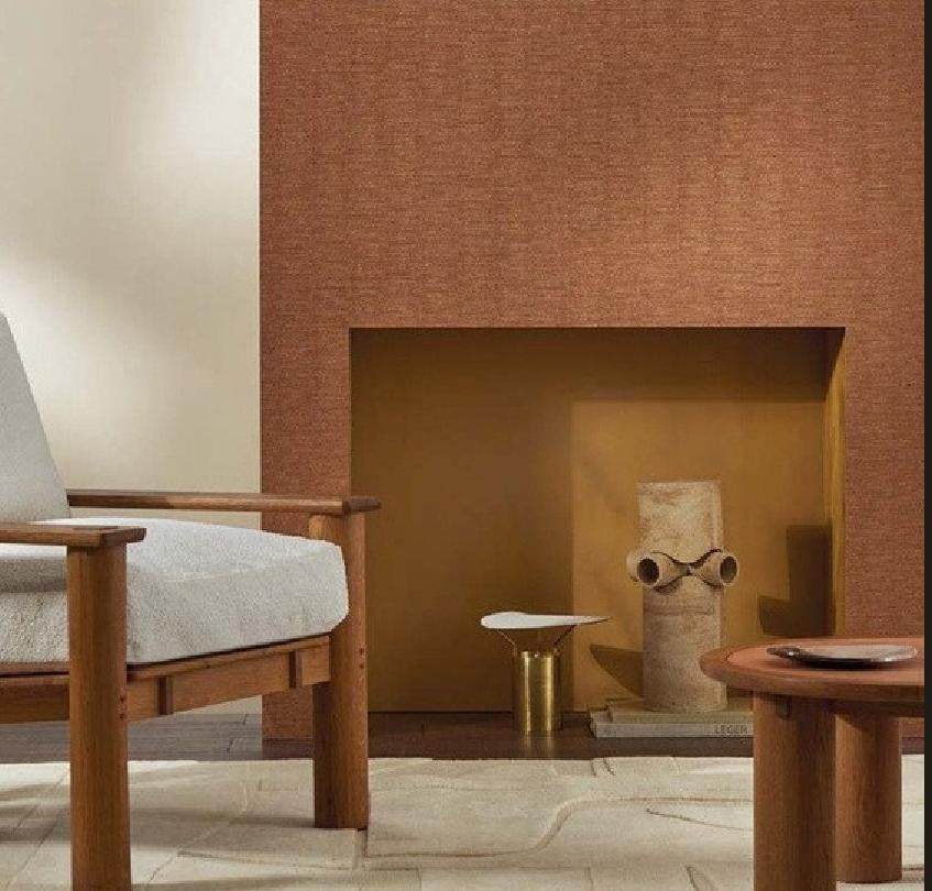 A styled interior scene showing a textured terracotta-brown Nerikomi wallpaper installed on a fireplace wall, alongside a vertical product information panel with color swatches and product details.